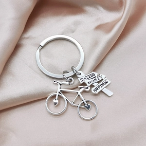 Silver bicycle keychain with Success Money Happiness signs on beige silk background
