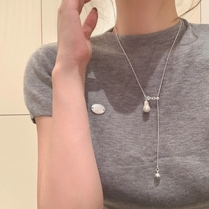 Gros plan d'un collier chaîne à billes argenté avec perle baroque et pendentif en métal