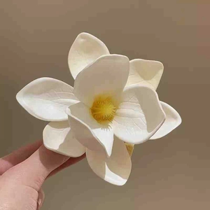 Close-up of a white plumeria flower hair clip held by hand showing petal texture