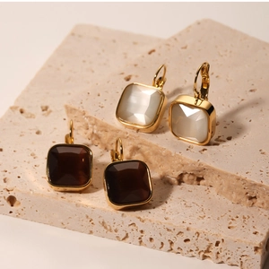 Detail of square vintage lever-back earrings with opal and brown stones on textured stone