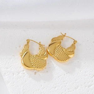 Detail of gold geometric hollow braided texture stainless steel earrings on white surface