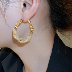 Close-up of golden twisted hoop earrings with textured finish on model ear
