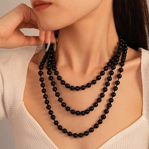 Close-up of triple-layered black pearl long necklace on model with white knit sweater