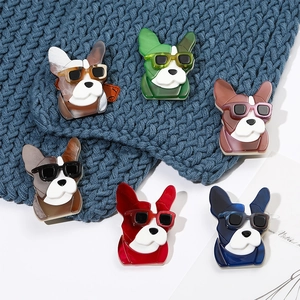 Close-up of cute acrylic cartoon puppy brooches with sunglasses on blue knitted fabric