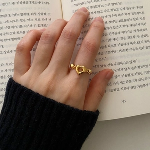Close-up of a gold heart ring with beaded band worn by a model over an open book