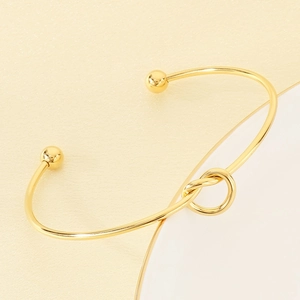 Detailed view of golden knot open cuff bracelet with polished finish and spherical ends