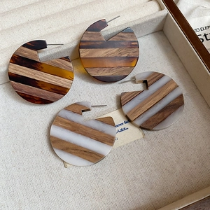 Detailed close-up of large round C-shaped wooden and resin earrings in a linen display box