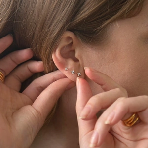 Close-up of three sparkling gold S925 sterling silver flower stud earrings on model ear