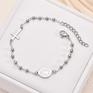 Macro shot of silver beaded bracelet featuring a religious cross and round medal charm