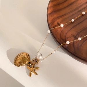 Golden ocean necklace with pearls, starfish and seashell pendants on a wooden tray