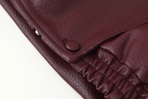 Macro shot of dark burgundy PU leather texture with matching snap buttons and elastic cuffs