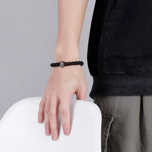 Detail of men's matte black beaded bracelet featuring a silver skull charm on wrist