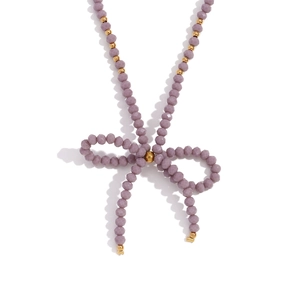 Purple beaded necklace featuring a crystal bow pendant and gold accents on white surface