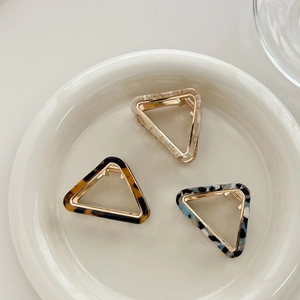 Three triangular acetate hair claws in tortoise shell and marble patterns on a white plate