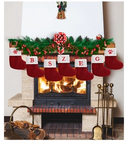 Detail of red knit Christmas stockings with white embroidered letters hanging on fireplace