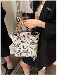 Detail of beige canvas bucket bag featuring black floral print and natural bamboo handles