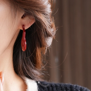 Macro shot of minimalist wine red fluid droplet earring with glossy enamel finish on ear