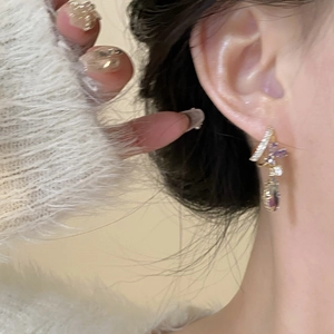Gros plan de boucles d'oreilles fleurs en zircon violet avec pompons dorés sur mannequin