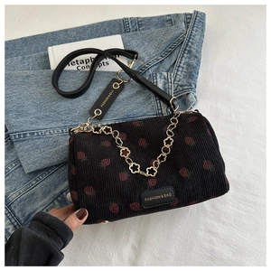 Detail of black corduroy shoulder bag with strawberry print and gold flower chain