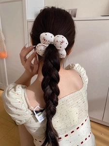 Rear view of a girl with braids wearing a white scrunchie with red bows and polka dots