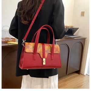 Red textured satchel with golden art print flap and metallic buckle on model