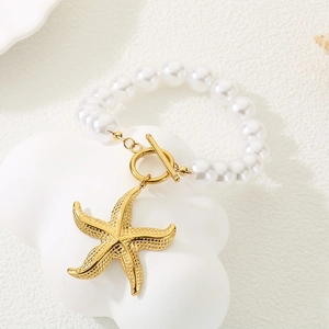 Vue détaillée du pendentif étoile de mer dorée et des perles blanches du bracelet d'été