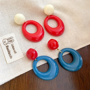 Détail de boucles d'oreilles ovales en résine rouge et bleu sur une surface en bois rustique