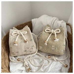 Detail of woven straw bucket bags with floral embroidery and tassel drawstring accents
