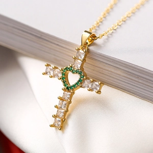 Gros plan du pendentif croix dorée avec zircons et un cœur vert au centre