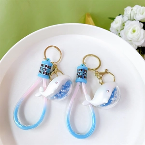 Cute dolphin whale keychain with blue glitter liquid and gold metal ring on white tray