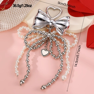 Silver bow keychain with white pearls and heart pendant, dimensions 14.5x9cm on pink base