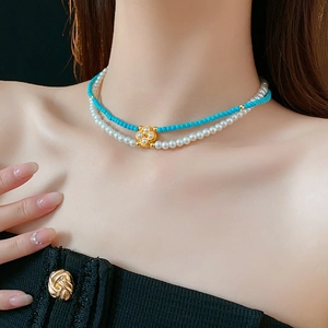 Dettaglio collana a due strati con perle, perline turchesi e ciondolo a quadrifoglio