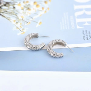 Elegant silver textured C-shaped hoop earrings on aesthetic floral background