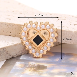 Elegant gold heart brooch with white pearls and black center on a stone surface