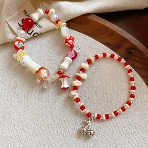 Handmade beaded bracelet set with ceramic cherry and apple pendants on a rustic wooden tray