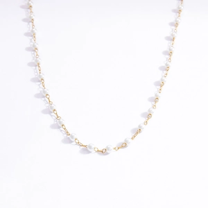 Detail view of thin gold chain necklace with small white pearls on a white background