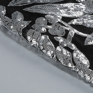 Détail macro des broderies de paillettes argentées sur un tissu en maille noire
