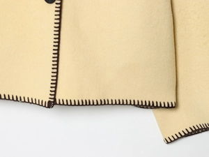 Detail of beige wool texture coat with dark brown decorative stitching on the hem