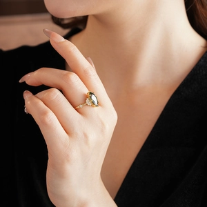 Dettaglio di un anello dorato con gemma verde taglio marquise e piccoli cristalli