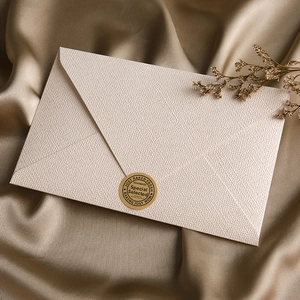 Detail of a beige textured paper envelope with a gold seal on a brown silk background