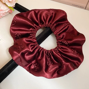 Vue détaillée du chouchou en satin bordeaux avec texture florale de roses en relief