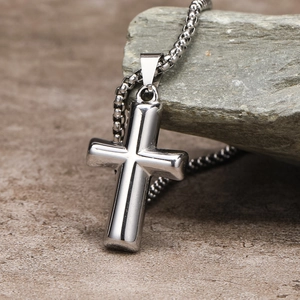 Detailed close-up of a silver polished stainless steel cross pendant on stone