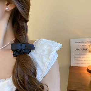 Detail of a black satin bow scrunchie with a pearl accent worn in a ponytail