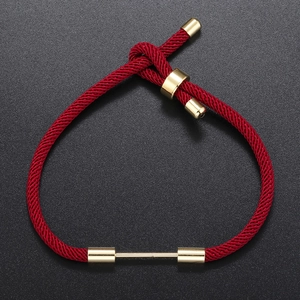 Adjustable red braided rope bracelet with polished gold metal hardware on black background