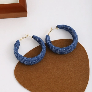 Detail shot of vintage denim-wrapped hoop earrings on a minimalist brown base cloth