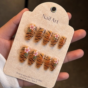 Detail of press-on nails with tiger print and 3D floral accents on amber base