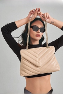 Macro shot of V-shaped quilted texture and gold chain on beige faux leather bag