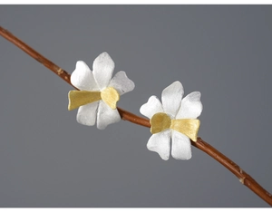 Macro shot of bicolored petal stud earrings in silver and gold on a twig