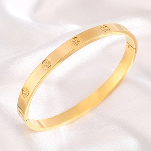 Macro shot of gold stainless steel bangle with circular carvings on white satin background