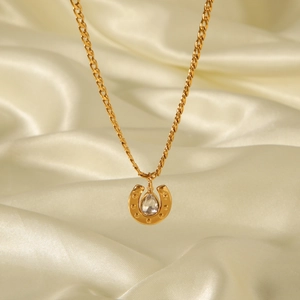Detailed macro view of 18k gold horseshoe pendant with zircon on a Cuban link chain
